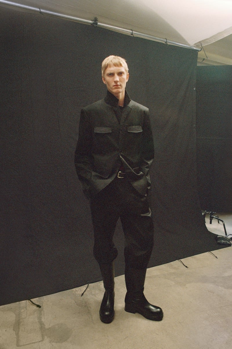 Pierrick Grégoire in a jacket with contrast flap pockets, belted trousers, and chunky leather boots in a studio