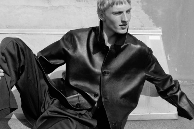 Black-and-white photo of Pierrick Grégoire reclining in a leather jacket and pleated trousers