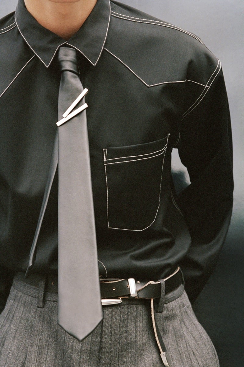 Pierrick Grégoire in a western shirt with contrast topstitching, a sleek tie with two tie bars, and a leather belt over herringbone trousers