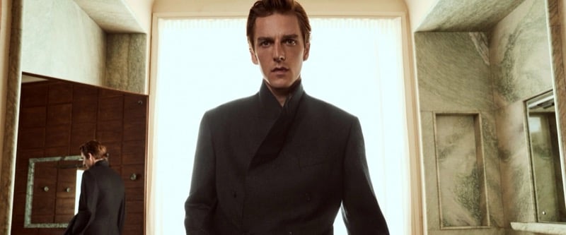 Quentin Demeester facing the camera in a double-breasted jacket inside a marble-walled room with a bright window behind him