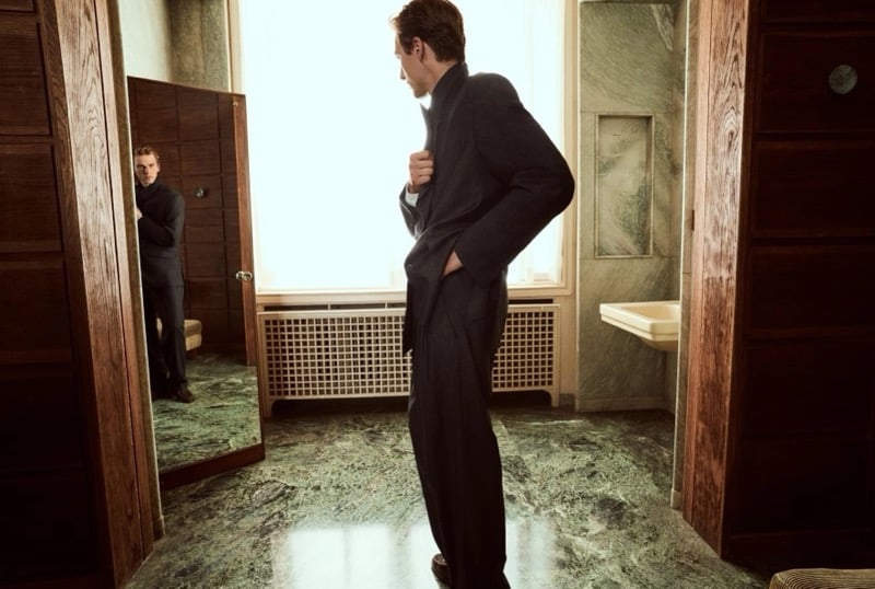 Quentin Demeester standing on a green marble floor and turning toward a mirror in a tailored jacket and wide-leg trousers