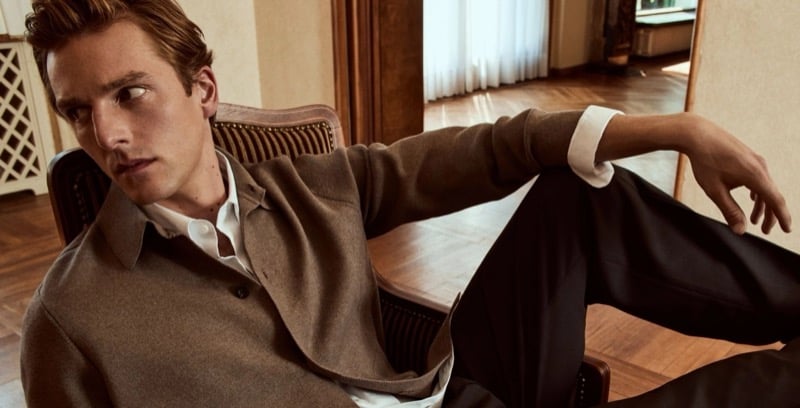 Quentin Demeester seated in a cane-back chair in a brushed overshirt layered over a collared shirt, one leg raised
