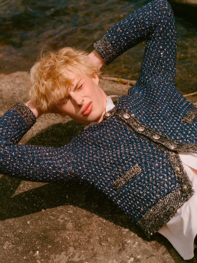Quinn McLachlan lies back on a lakeside rock in a sparkling blue tweed Dior cardigan with metallic trim and jeweled buttons
