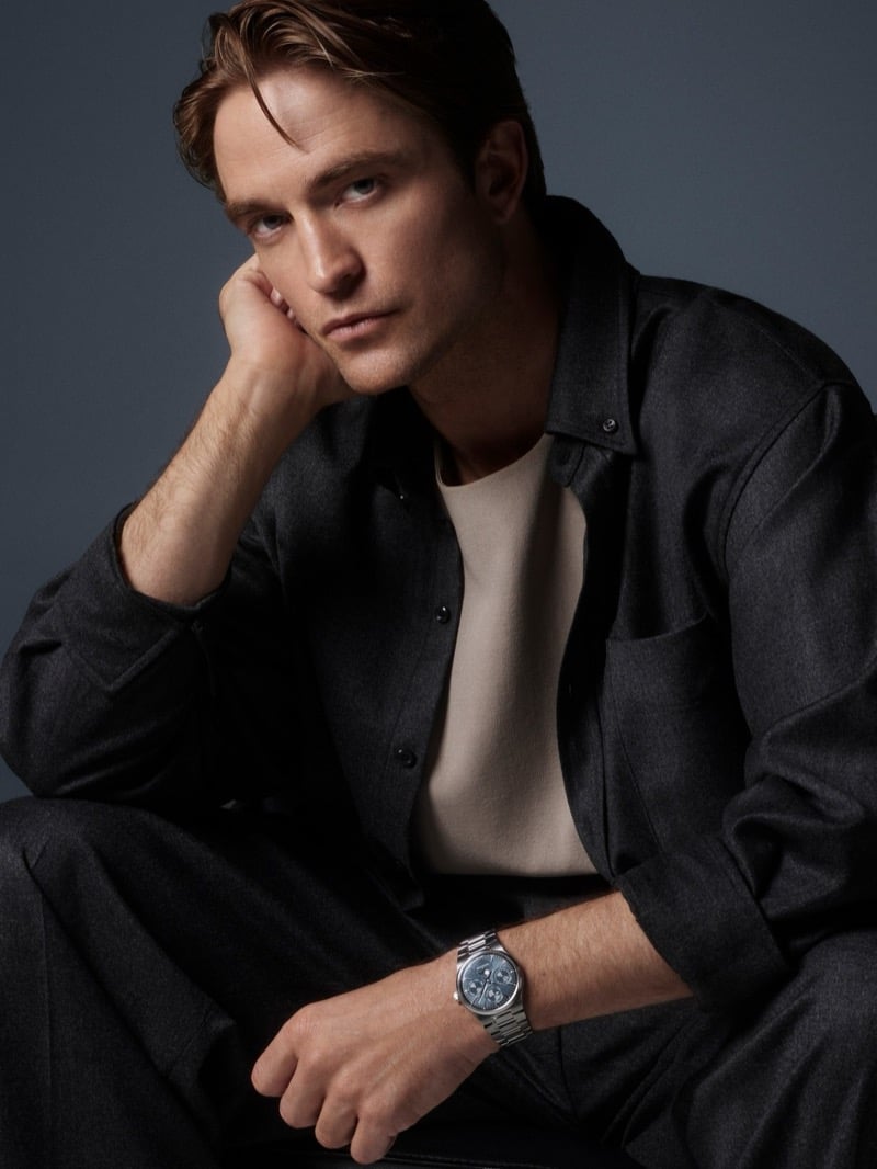 Robert Pattinson seated with his head resting on his hand, wearing an overshirt, crewneck, and a steel Jaeger-LeCoultre watch