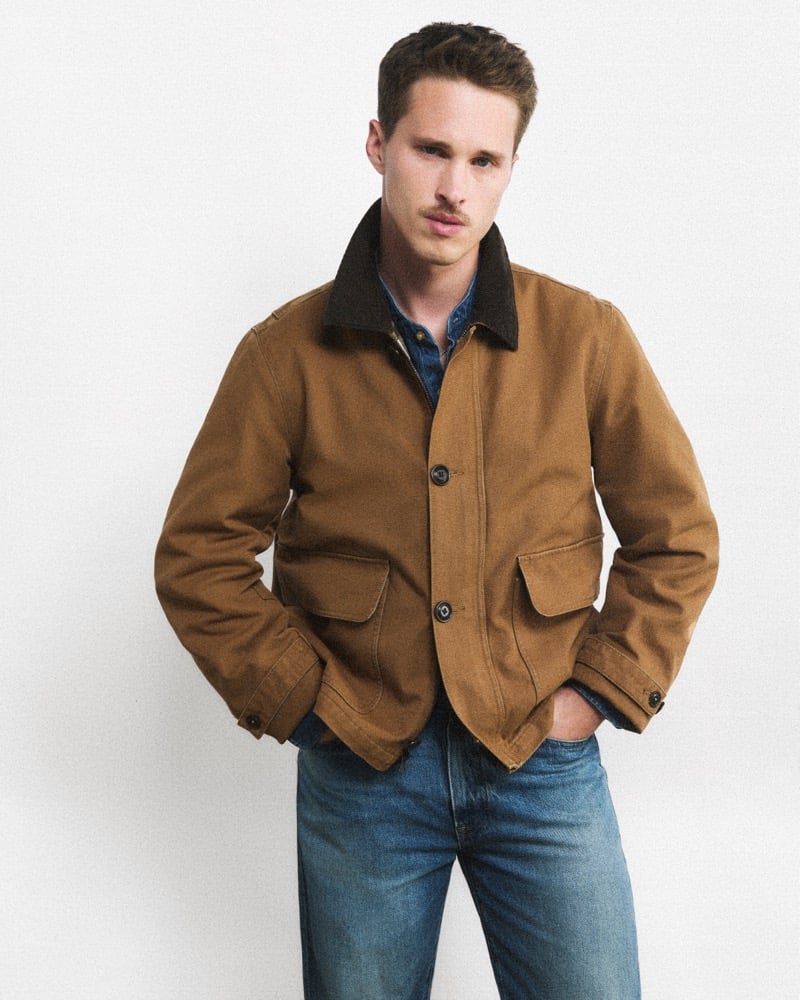 Ryan Beatty in a tan canvas J.Crew Barn Jacket, denim shirt, and jeans with hands in pockets