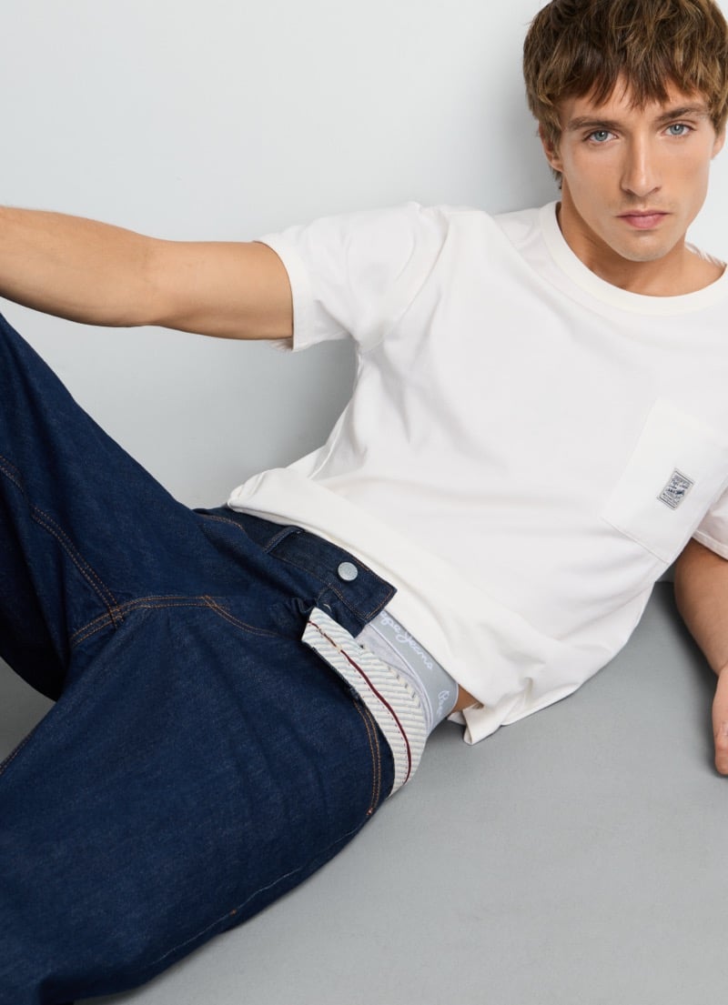 Samuel Curtis reclines in a pocket tee, showing the Pepe Jeans waistband tab on the Dalston selvedge jean