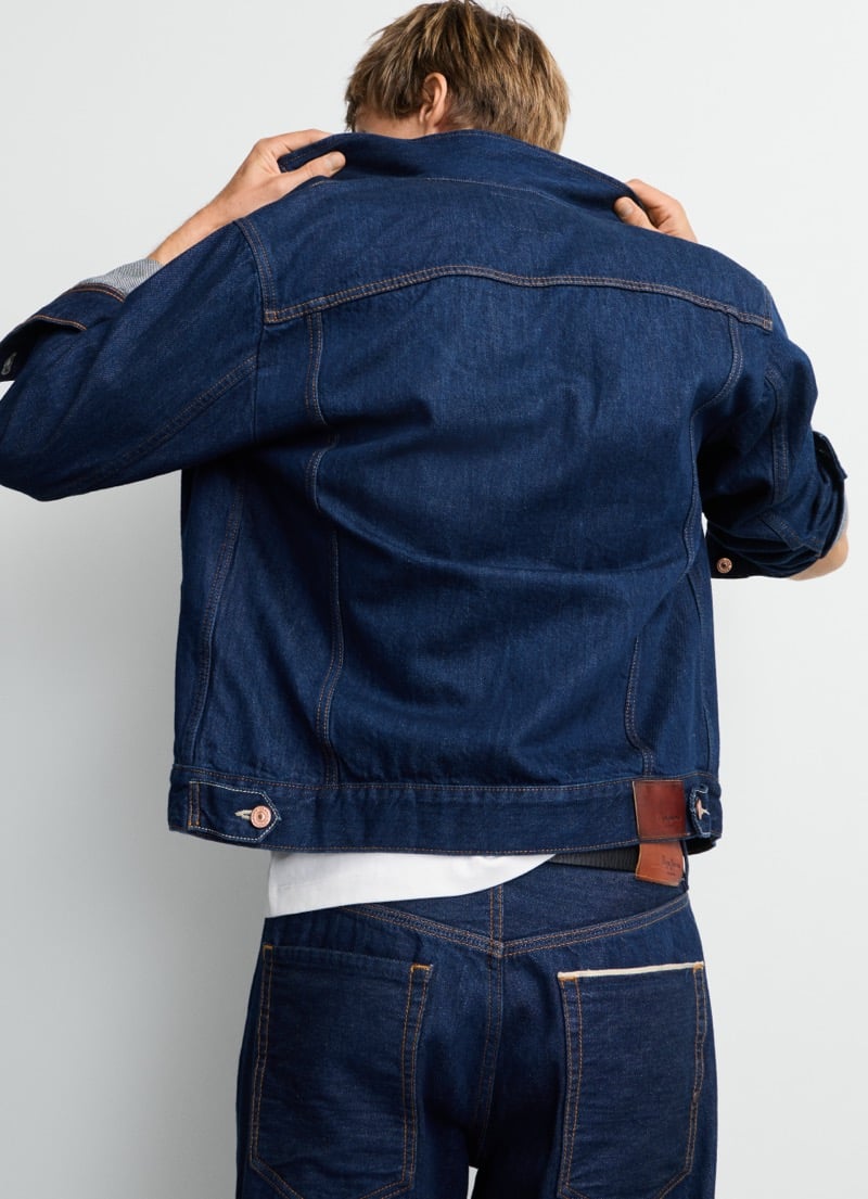 Samuel Curtis adjusts the collar of Pepe Jeans' selvedge trucker jacket, showing the leather brand patch at the hem