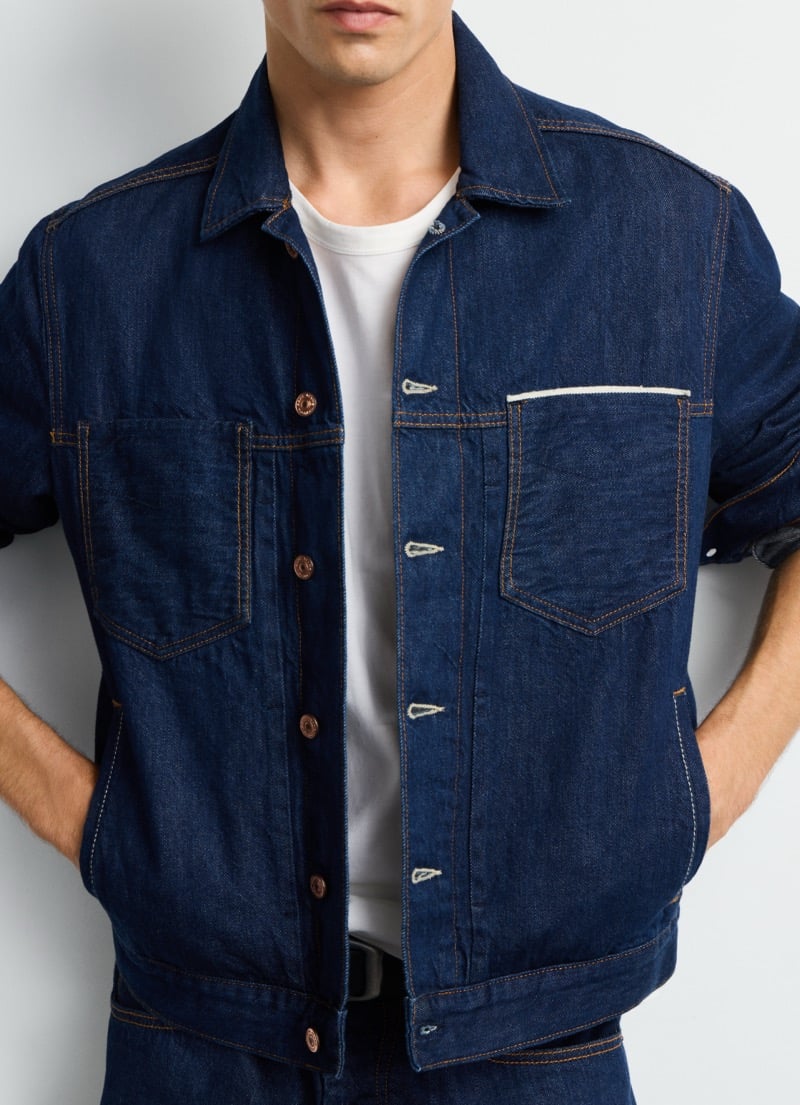 Detail of the chest pockets and snap buttons on Pepe Jeans' selvedge trucker jacket, worn open over a white tee