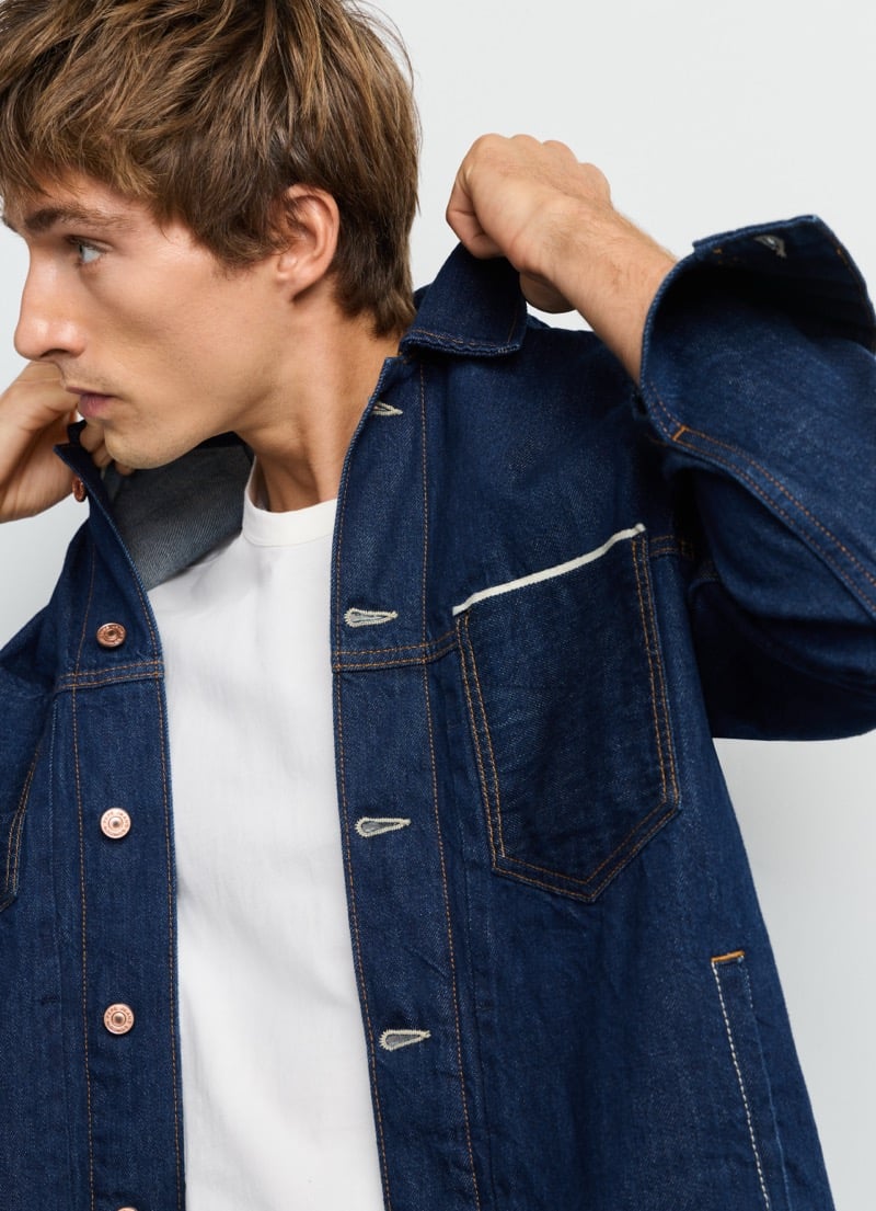 Close-up of Pepe Jeans' selvedge trucker jacket chest pocket and copper hardware, worn by Samuel Curtis over a white tee