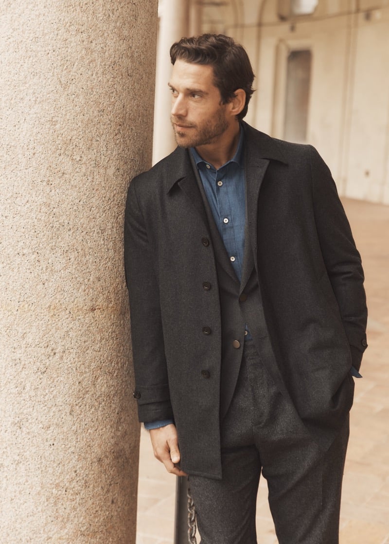 Simone Bredariol against a stone column in a charcoal overcoat over a suit and a denim shirt, for Boglioli's fall-winter 2026 campaign