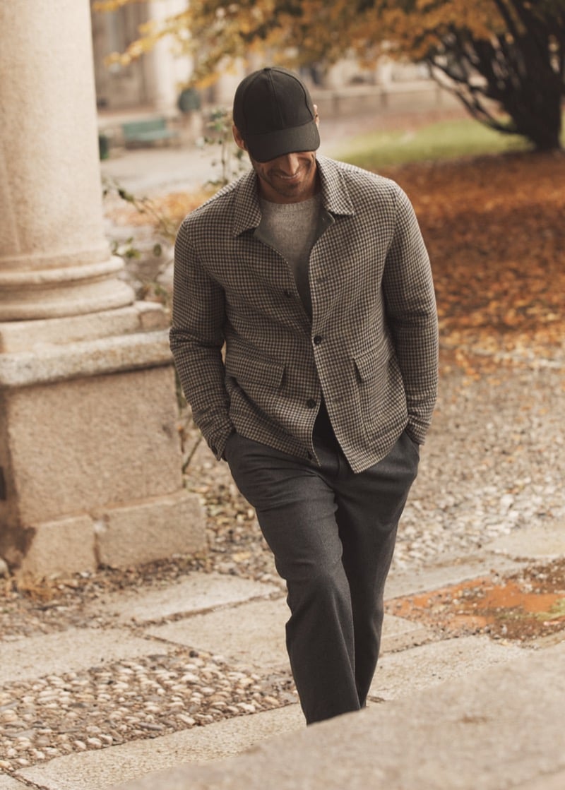 Simone Bredariol in a checked wool overshirt over a gray sweater with gray trousers and a cap, for Boglioli's fall-winter 2026 campaign