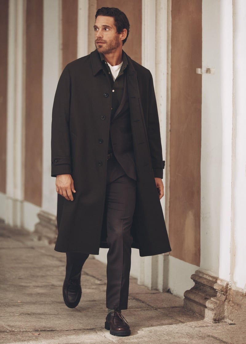 Simone Bredariol walking under a portico in a dark overcoat over a suit and an olive overshirt, for Boglioli's fall-winter 2026 campaign