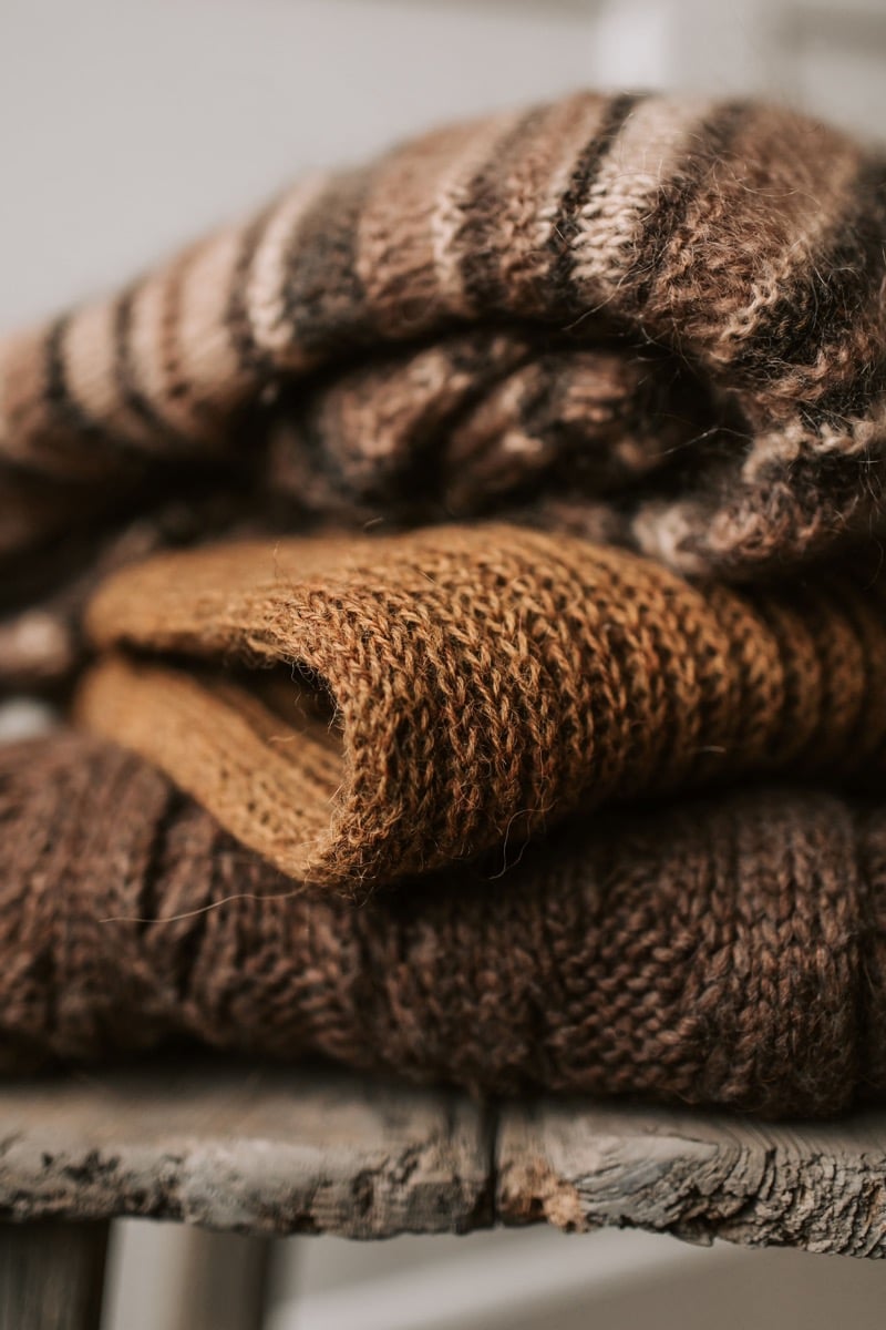 A close-up of folded brown wool knit sweaters stacked on a weathered wooden bench
