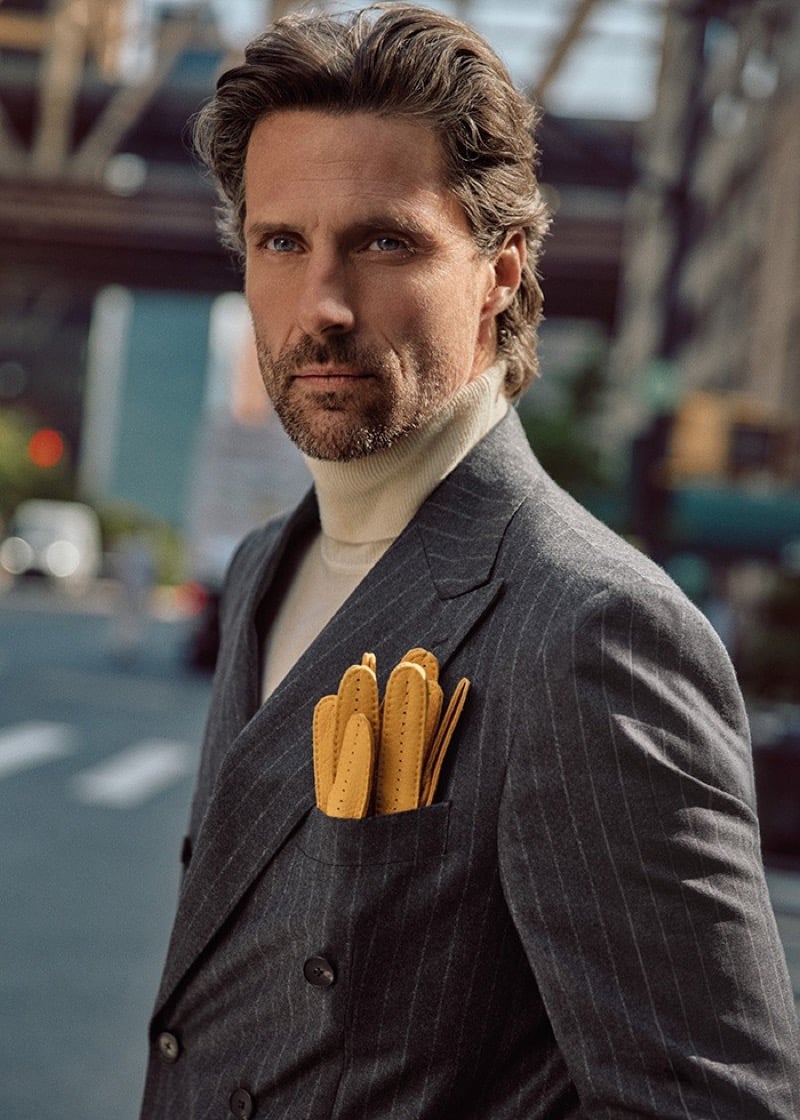 Tommy Dunn in a gray pinstripe double-breasted suit and cream turtleneck with yellow driving gloves tucked in the breast pocket