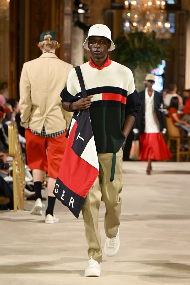 A model in a bucket hat and colorblock sweater with a Tommy Hilfiger flag-logo tote bag and khaki trousers, for Tommy Hilfiger's spring 2027 collection
