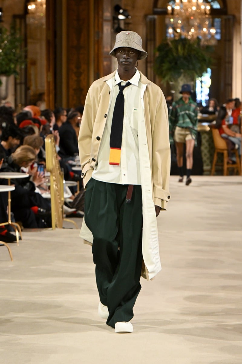 A model in a bucket hat and beige trench coat with dark green wide-leg trousers and a knit tie, for Tommy Hilfiger's spring 2027 collection