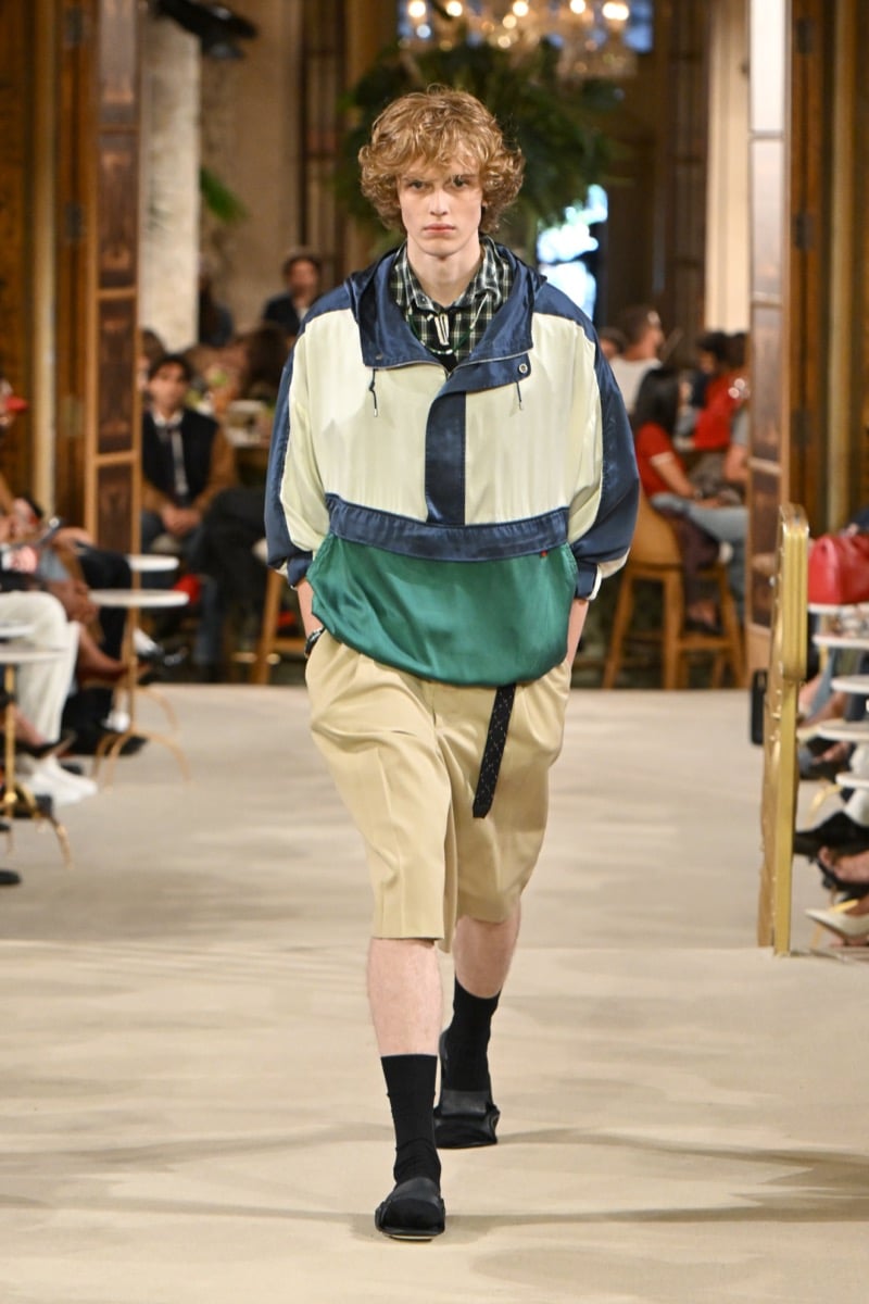 A model in a colorblock hooded anorak over a plaid collar shirt, with khaki shorts and loafers, for Tommy Hilfiger's spring 2027 collection