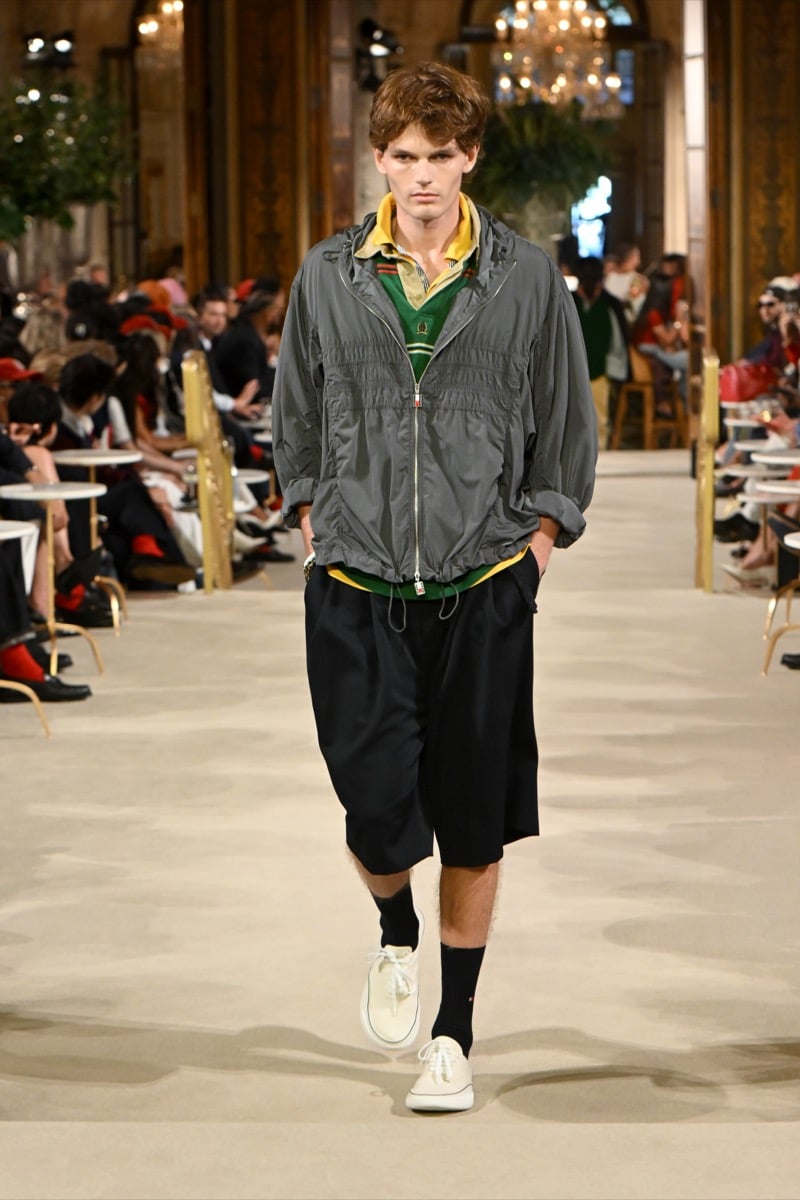 A model in a gray zip jacket over a striped polo, with shorts and white sneakers, for Tommy Hilfiger's spring 2027 collection