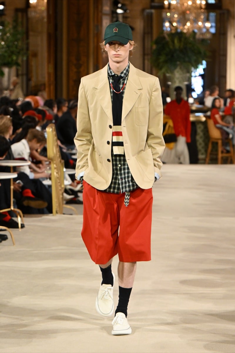 A model in a green baseball cap and beige blazer over a plaid shirt, with red shorts and white sneakers, for Tommy Hilfiger's spring 2027 collection