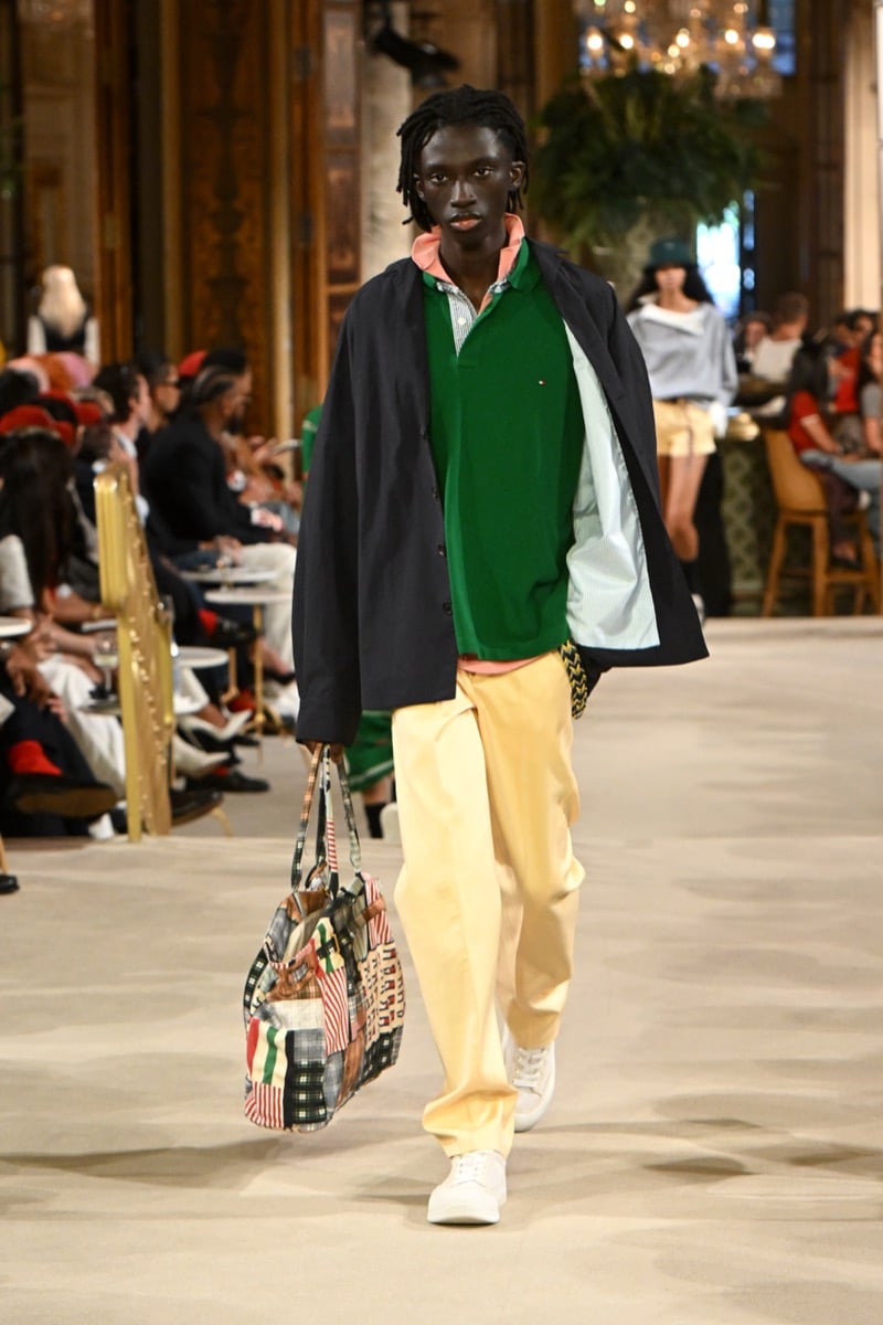 A model in an overshirt worn open over a green polo, with yellow wide-leg trousers and a flag-print tote bag, for Tommy Hilfiger's spring 2027 collection