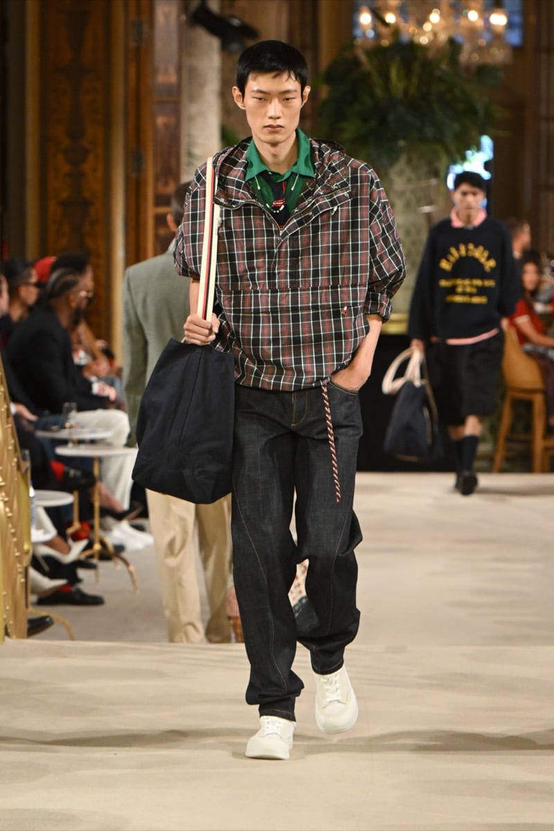 A model in a plaid half-zip jacket over a green-collar polo, with dark denim jeans and a tote bag, for Tommy Hilfiger's spring 2027 collection