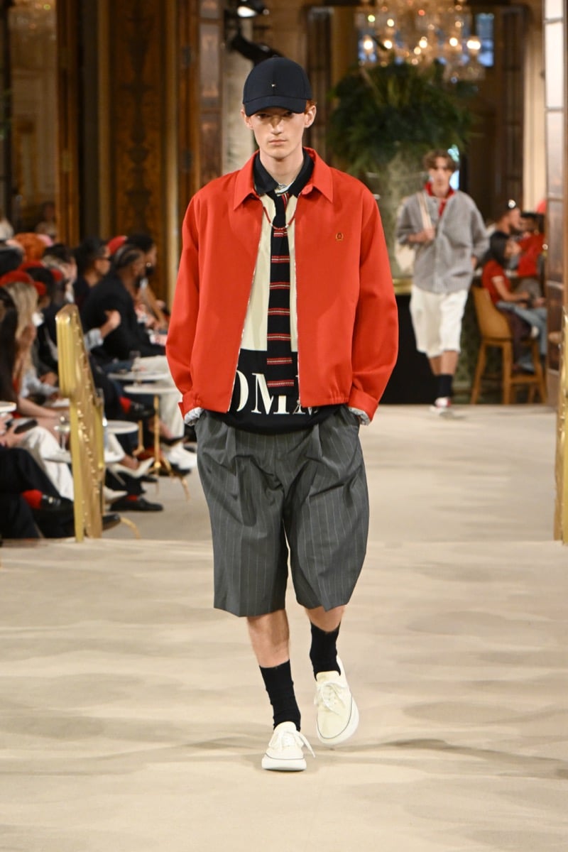 A model in a cap and red jacket over a striped wordmark sweater, with pinstripe shorts, for Tommy Hilfiger's spring 2027 collection
