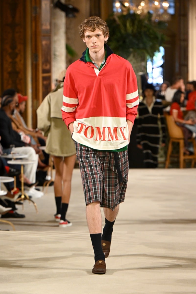 A model in a red rugby polo with a 'Tommy' wordmark and plaid shorts, styled with brown loafers, for Tommy Hilfiger's spring 2027 collection