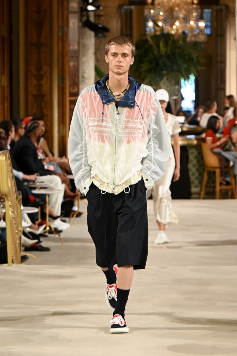A model in a sheer pastel bomber jacket layered over necklaces, with shorts and red-and-white sneakers, for Tommy Hilfiger's spring 2027 collection