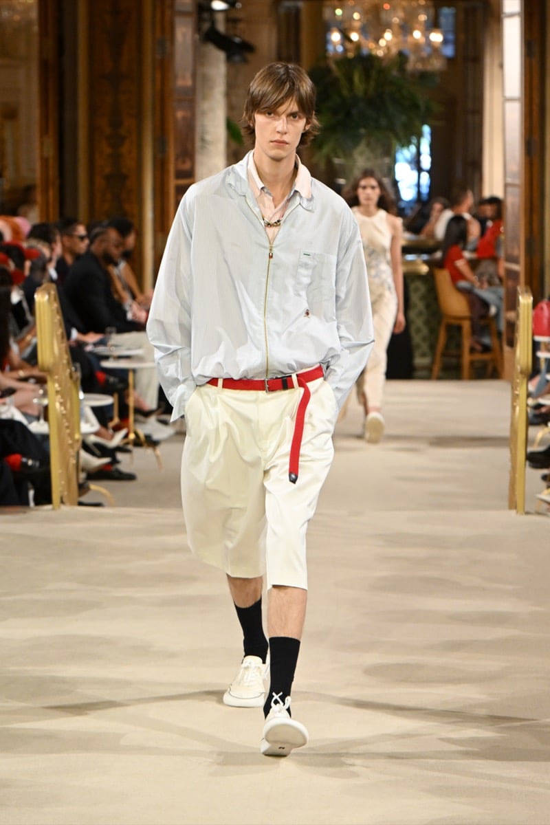 A model in a striped zip jacket over a pink collared shirt, with light-colored shorts and a red belt, for Tommy Hilfiger's spring 2027 collection