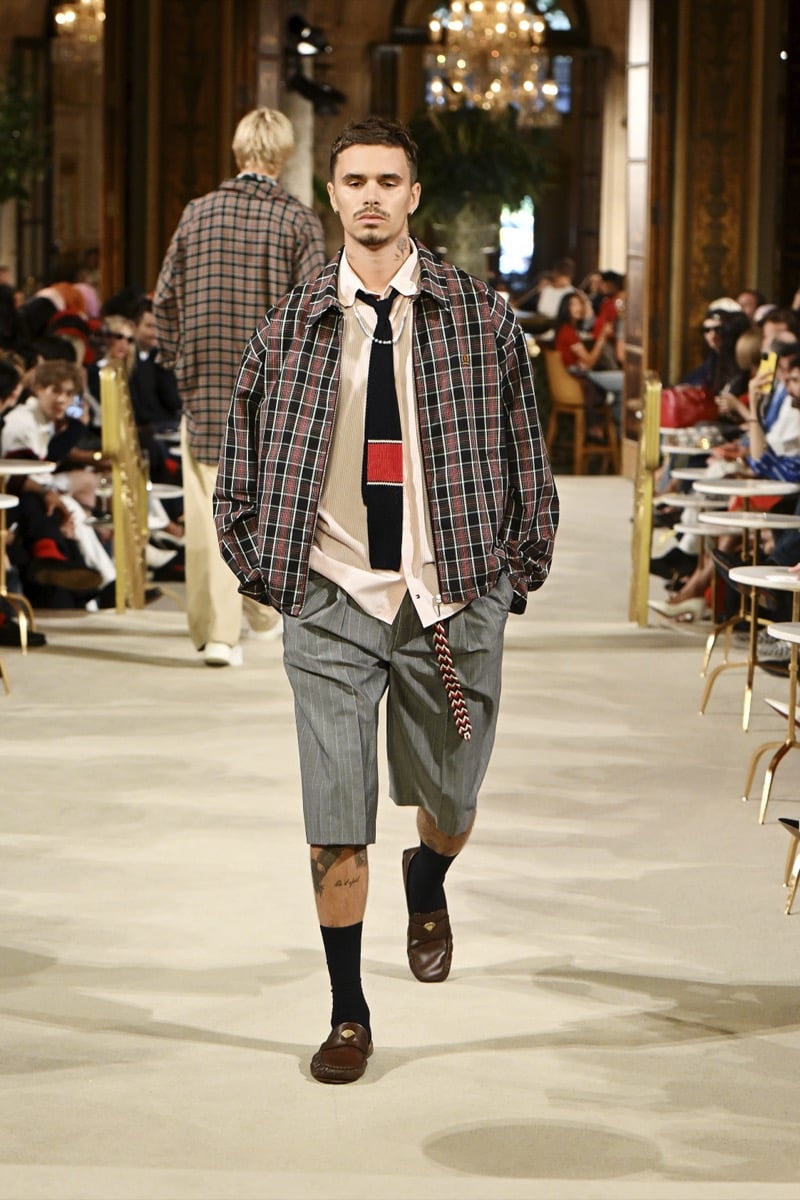 A model in a tartan plaid jacket over a striped shirt and knit tie, with shorts and brown loafers, for Tommy Hilfiger's spring 2027 collection