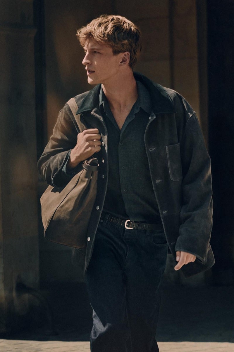 Vasko Luyckx walks with a canvas bag slung over his shoulder in a dark jacket and shirt for Zara's 90's Archive