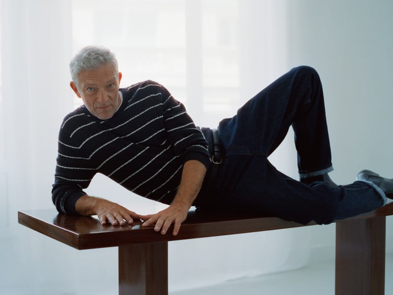 Vincent Cassel reclining on a wooden bench in a striped sweater, belted dark-wash jeans, and boots for Mango