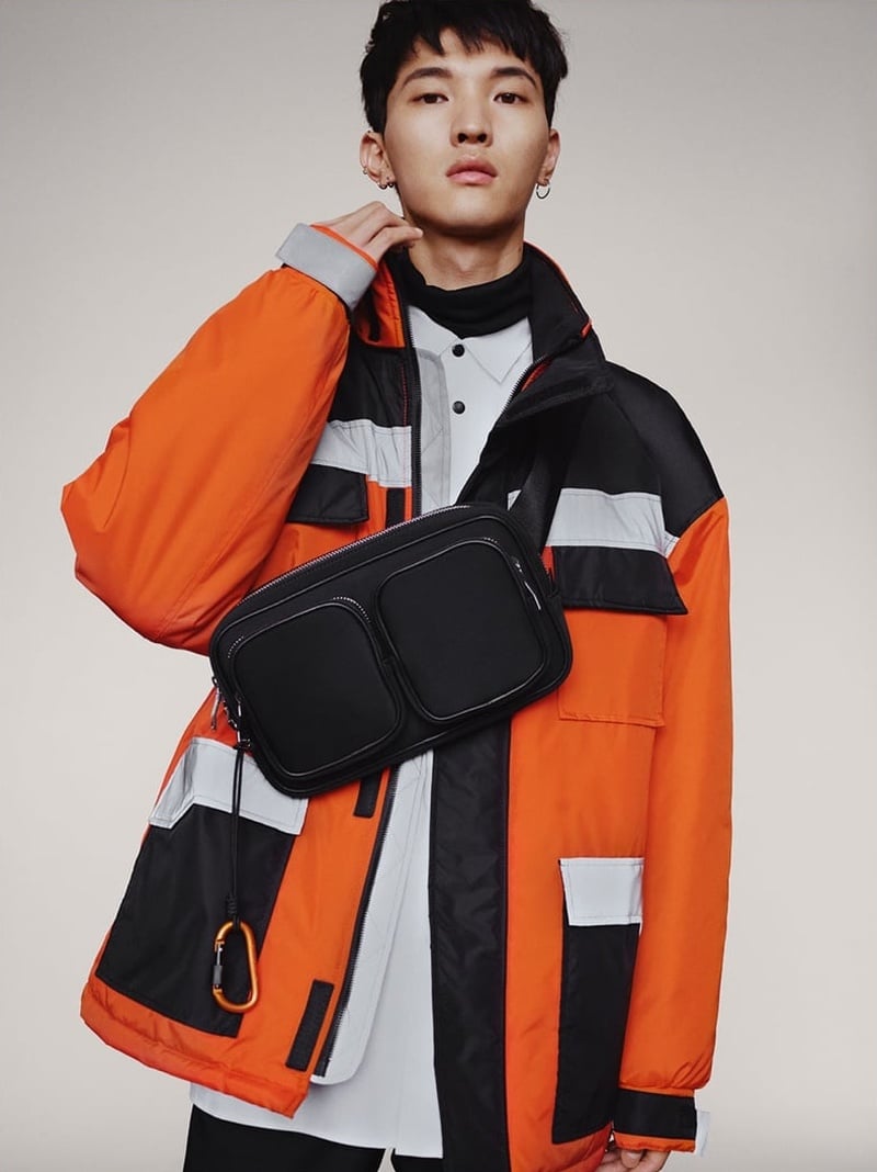 Jeon June wears a black belt bag across an orange and black technical jacket for Zara fall 2018.