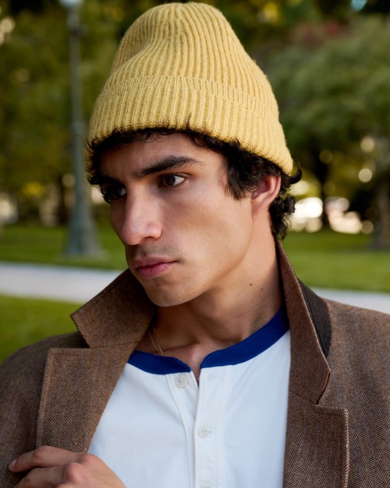 Duncan Yair wears Abercrombie & Fitch’s essential rib beanie in gold with a brown blazer and white henley.