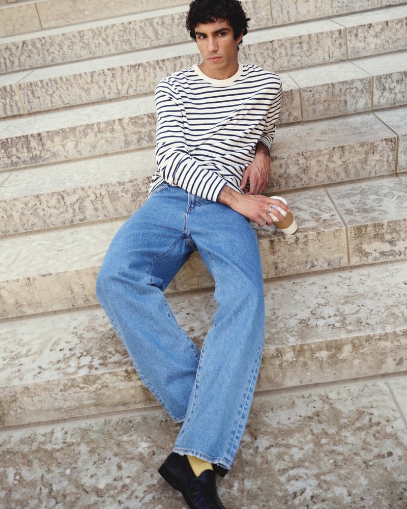 Duncan Yair wears Abercrombie & Fitch’s striped long-sleeve heritage heavyweight tee with loose blue jeans on stone steps.