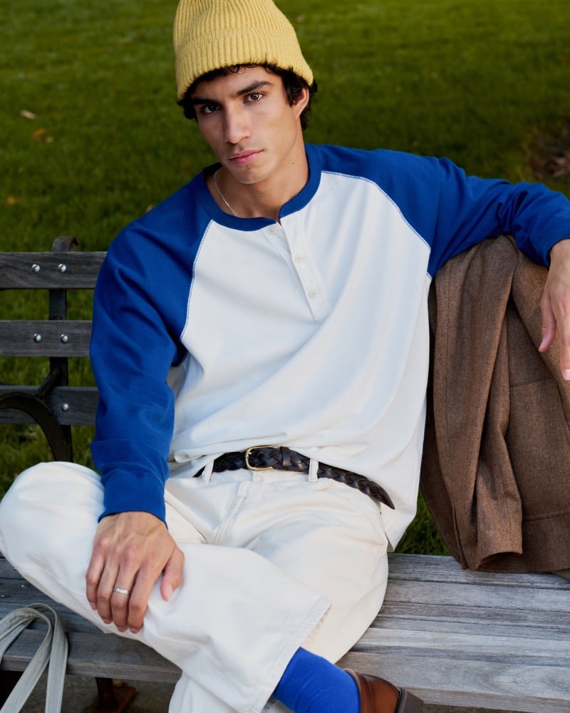 Duncan Yair relaxes on a park bench in Abercrombie & Fitch’s premium heavyweight 2.0 henley, white jeans, and a gold beanie.