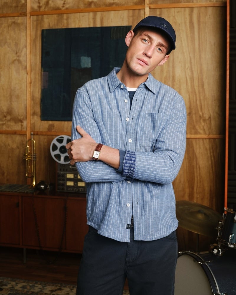 Aubrey O'Mahony wears a blue striped shirt and dark cap in a recording studio.