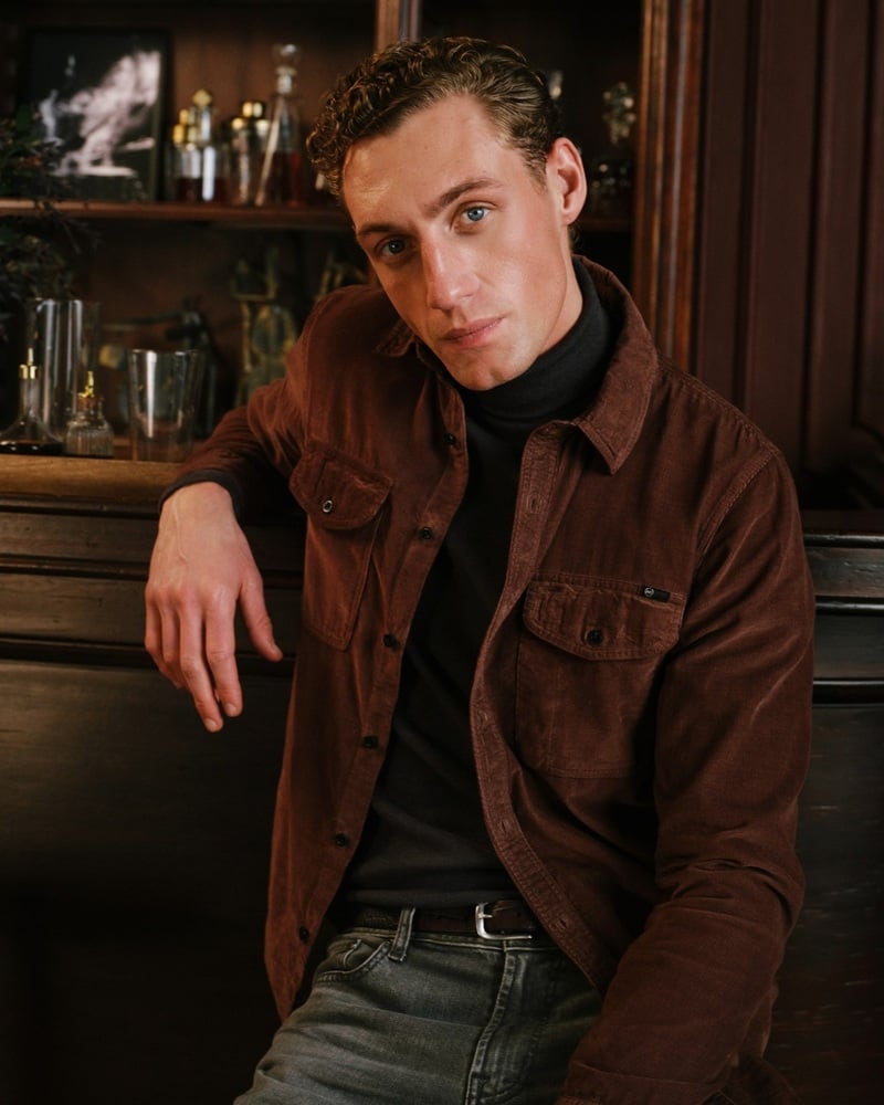 Aubrey O'Mahony wears a brown jacket over a black turtleneck at a bar.