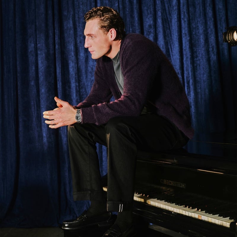 Aubrey O'Mahony sits at a piano in a deep purple cardigan and dark trousers.