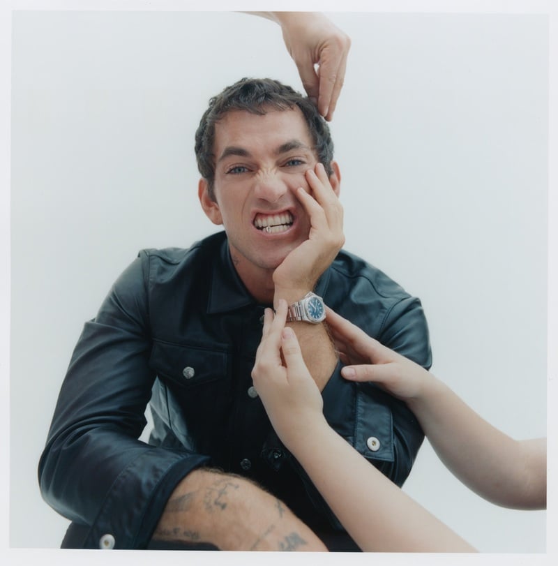 Alex Fine wears a leather jacket as hands reach into the frame to groom him.