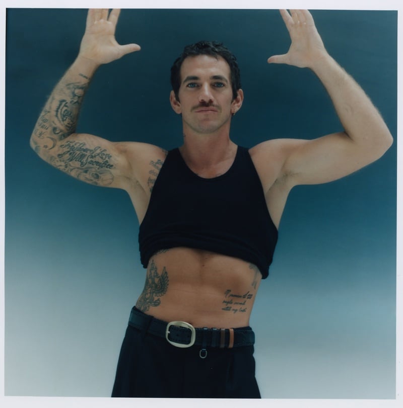 Alex Fine raises his arms in a cropped black top, black trousers, and an Isabel Marant belt.