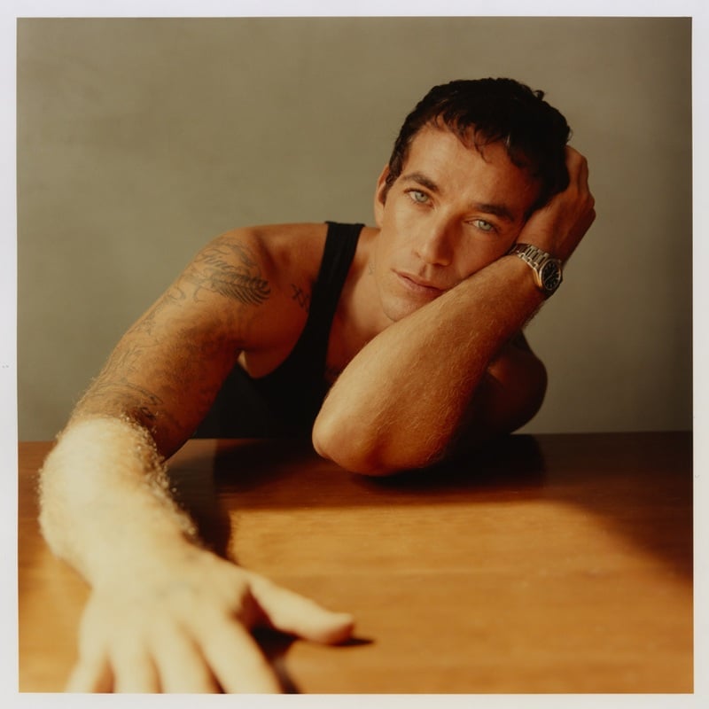 Alex Fine leans on a table in a black tank top, resting his head on one hand.