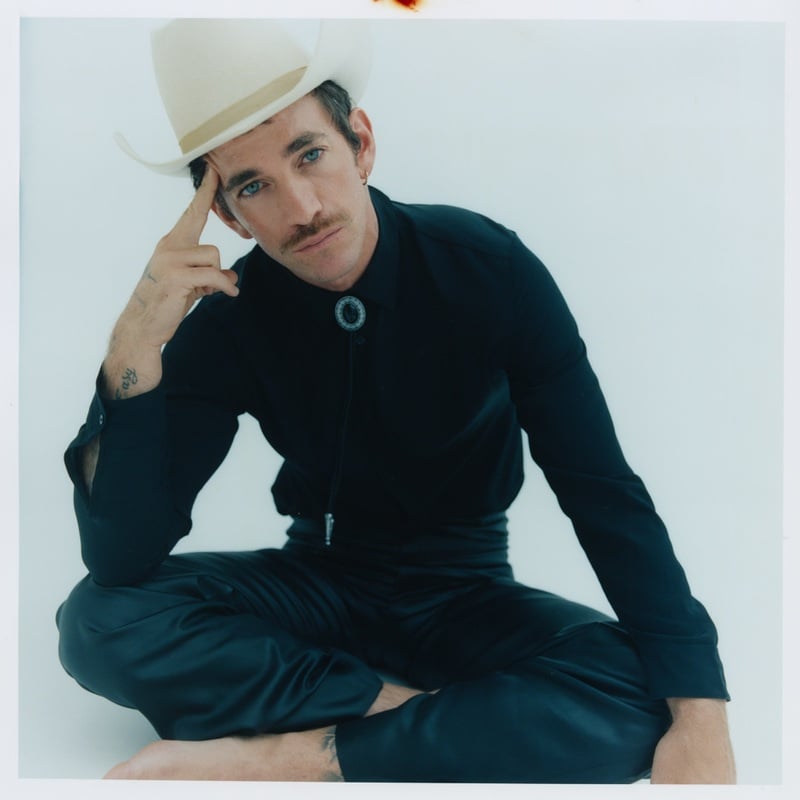 Alex Fine wears a white cowboy hat and bolo tie with a black Gucci shirt and trousers.