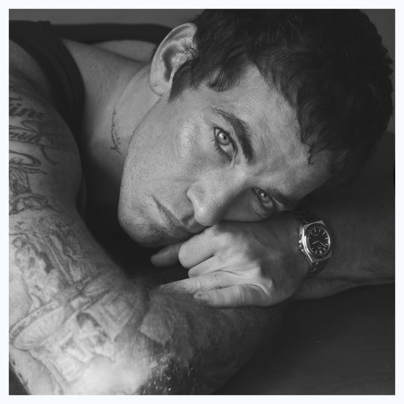 Alex Fine rests his head on his arm in a black-and-white portrait, wearing a tank top and IWC watch.
