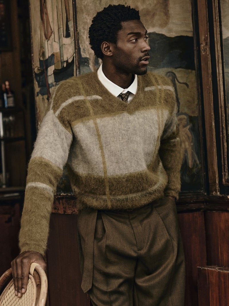 Halid Nuhu wears a patterned sweater tucked into pleated trousers with a white shirt.
