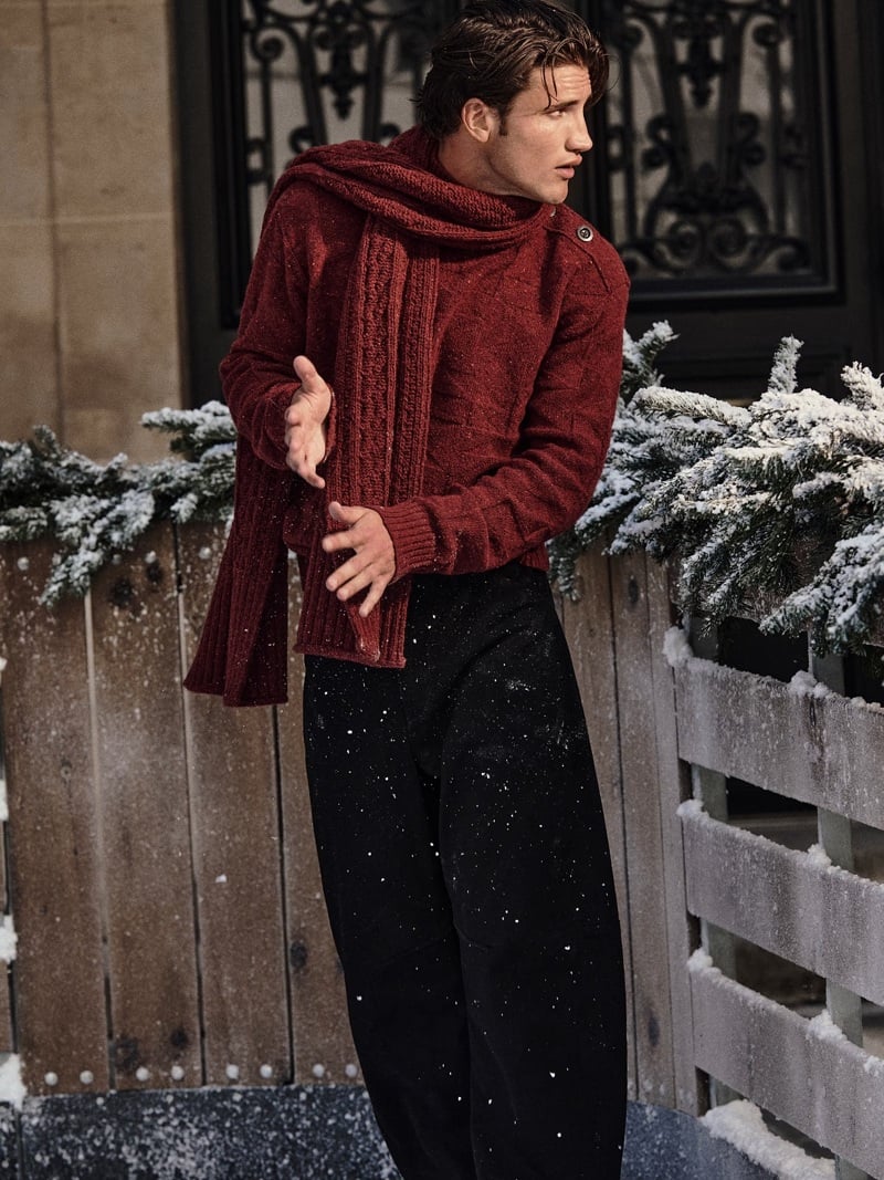 Max Knott wears a red cable-knit sweater and matching scarf on a snowy Paris street.