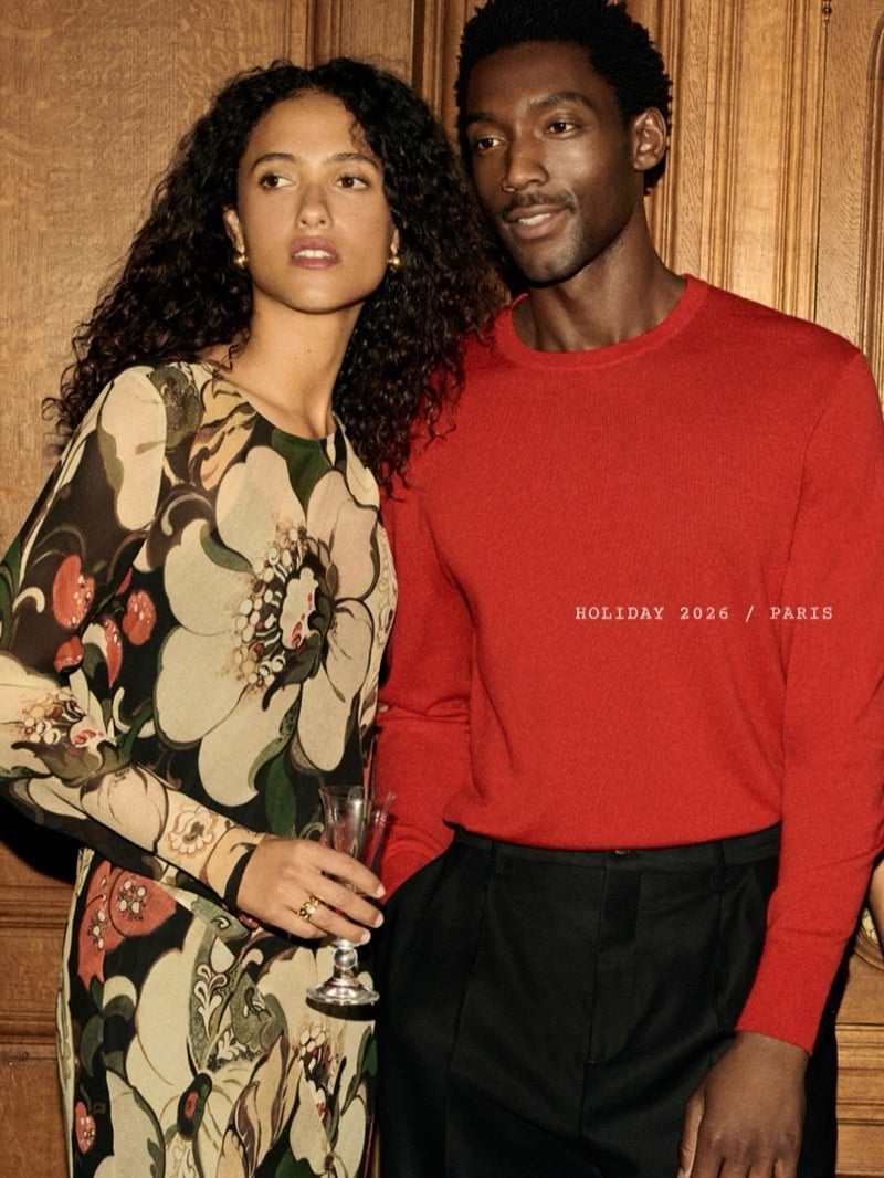 Halid Nuhu poses beside a woman in a floral dress, wearing a red sweater and black trousers.