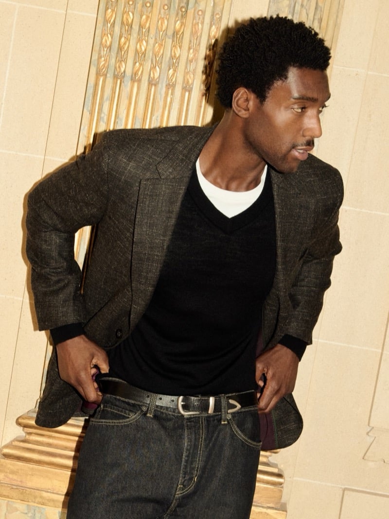 Halid Nuhu wears a brown wool-blend suit jacket over a black V-neck sweater and white shirt with jeans.