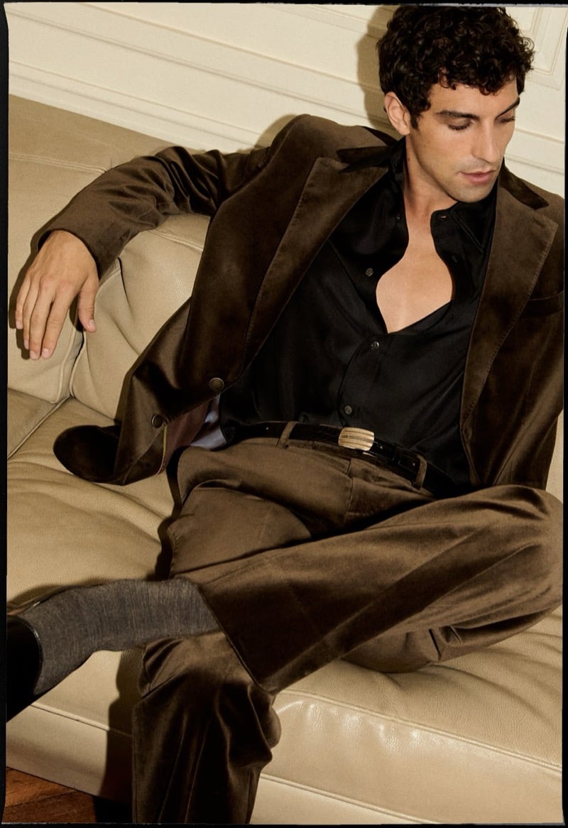 Francisco Faria reclines on a sofa in a brown velvet blazer and matching suit pants with a black shirt.