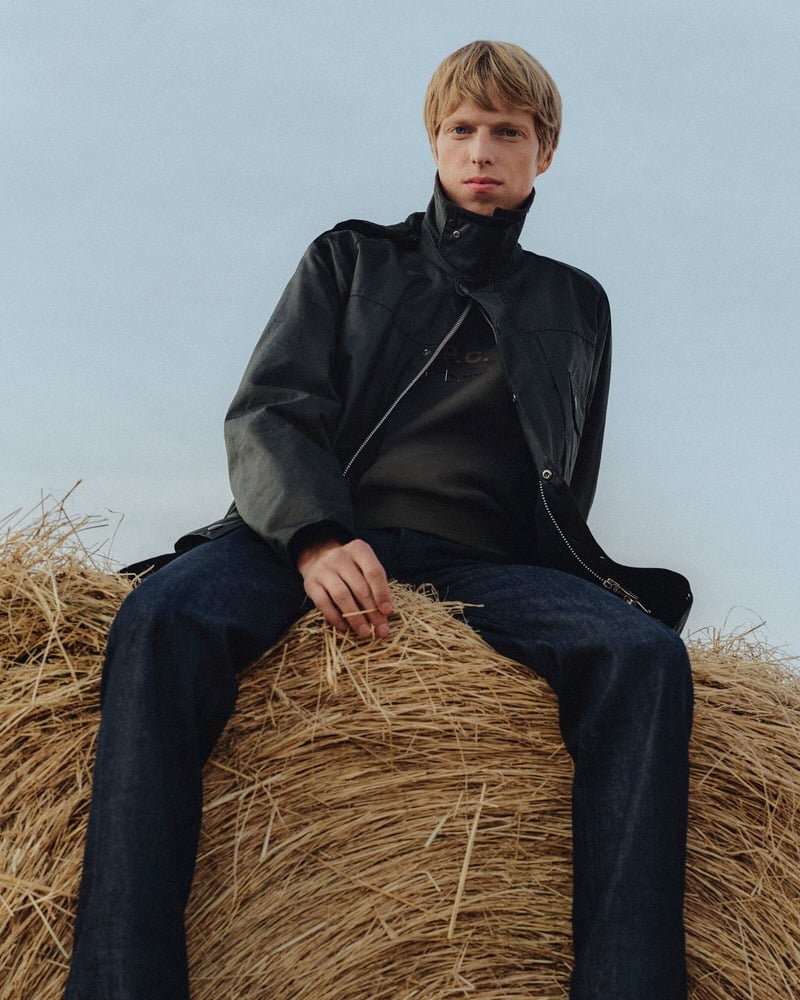 Joseph Uyttenhove sitting on a hay bale in a waxed jacket and dark jeans for Barbour x A.P.C.